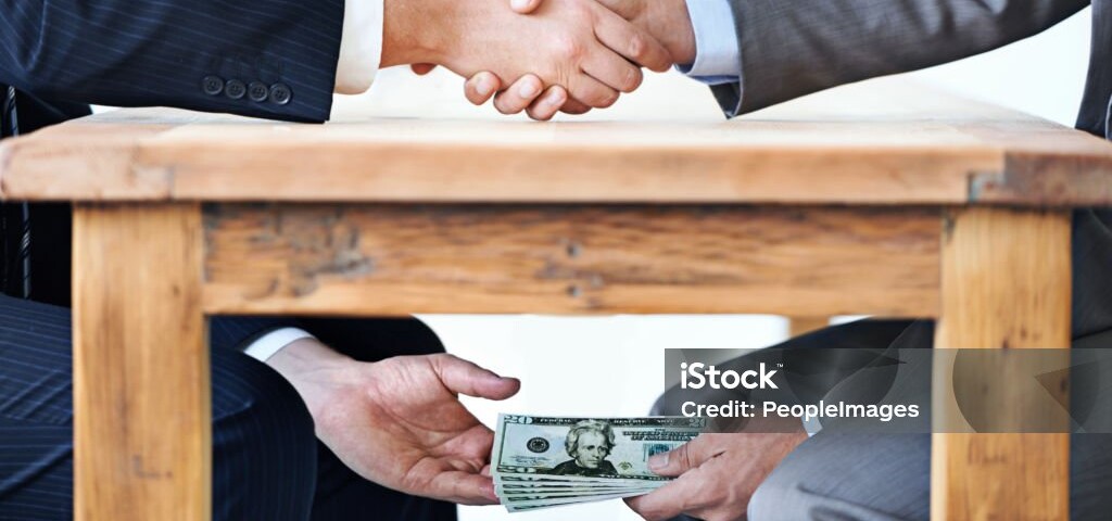 Cropped shot of two businessmen shaking hands while money passes hands under a table
