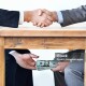 Cropped shot of two businessmen shaking hands while money passes hands under a table