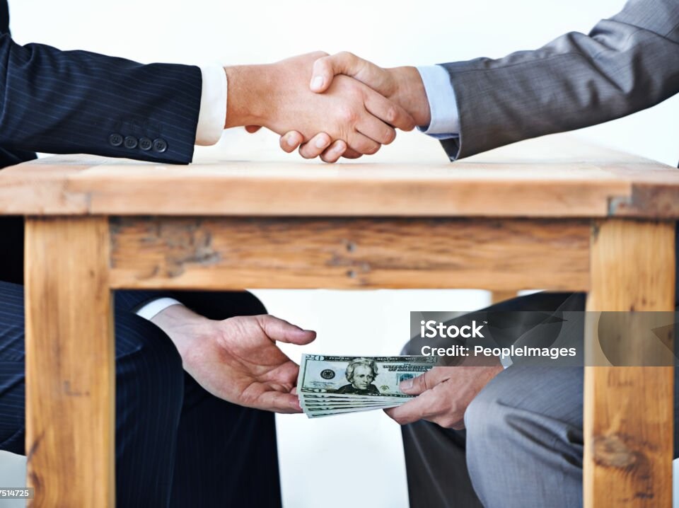 Cropped shot of two businessmen shaking hands while money passes hands under a table